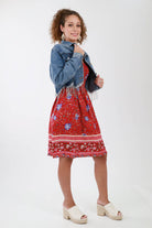 Red floral smocked dress with a fringe jean jacket, wood diamond earrings, and wedges